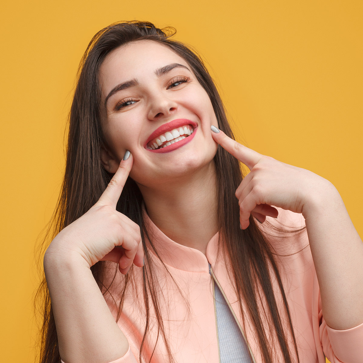 a young woman smiling really big pointing at her white teeth.
